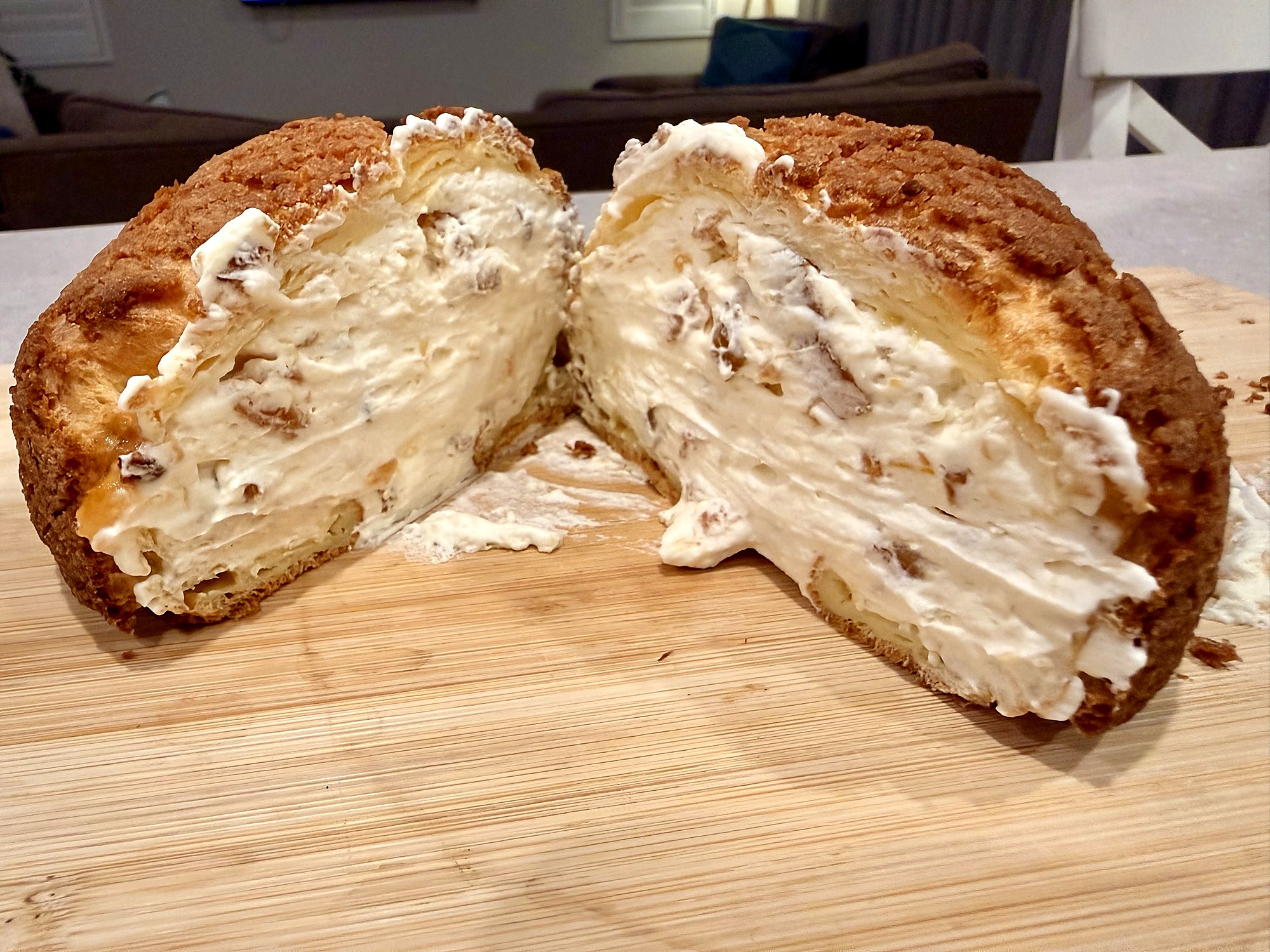 A choux bun cut in half on a wooden cutting board, revealing the marmalade chantilly filling: billowy white cream rippled with strands of orange peel and a glistening core of marmalade at the centre