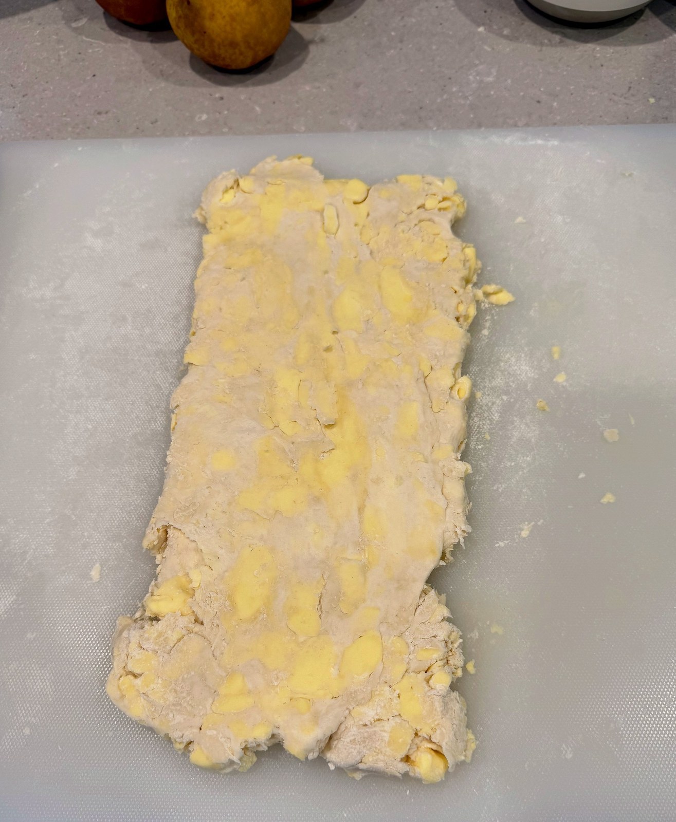 Rolled-out rough puff dough on a board, flecked through with flattened chunks of butter still visible as pale streaks across the surface